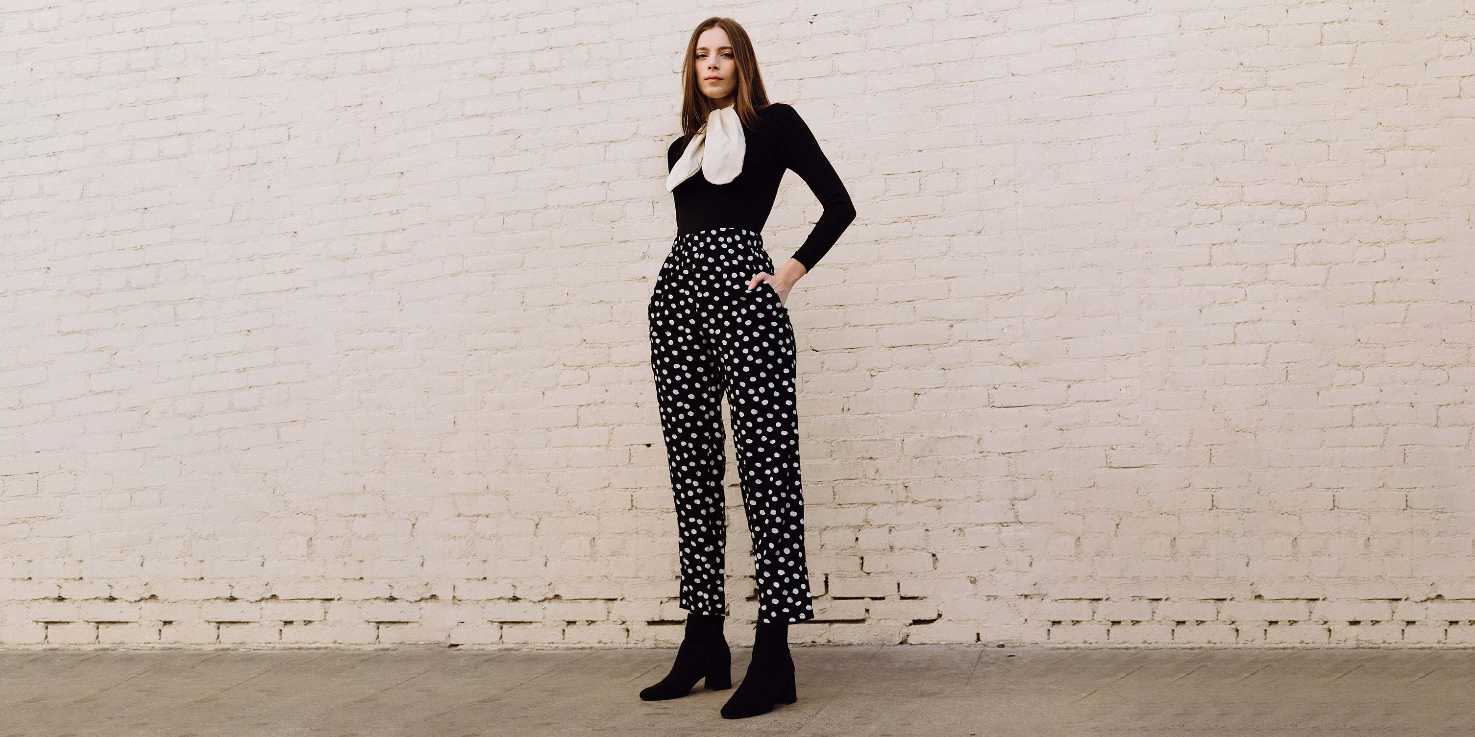 Stylish editorial photograph of a model wearing vintage polka dot pants & a 60s black & white ascot blouse from Flying Apple Vintage.